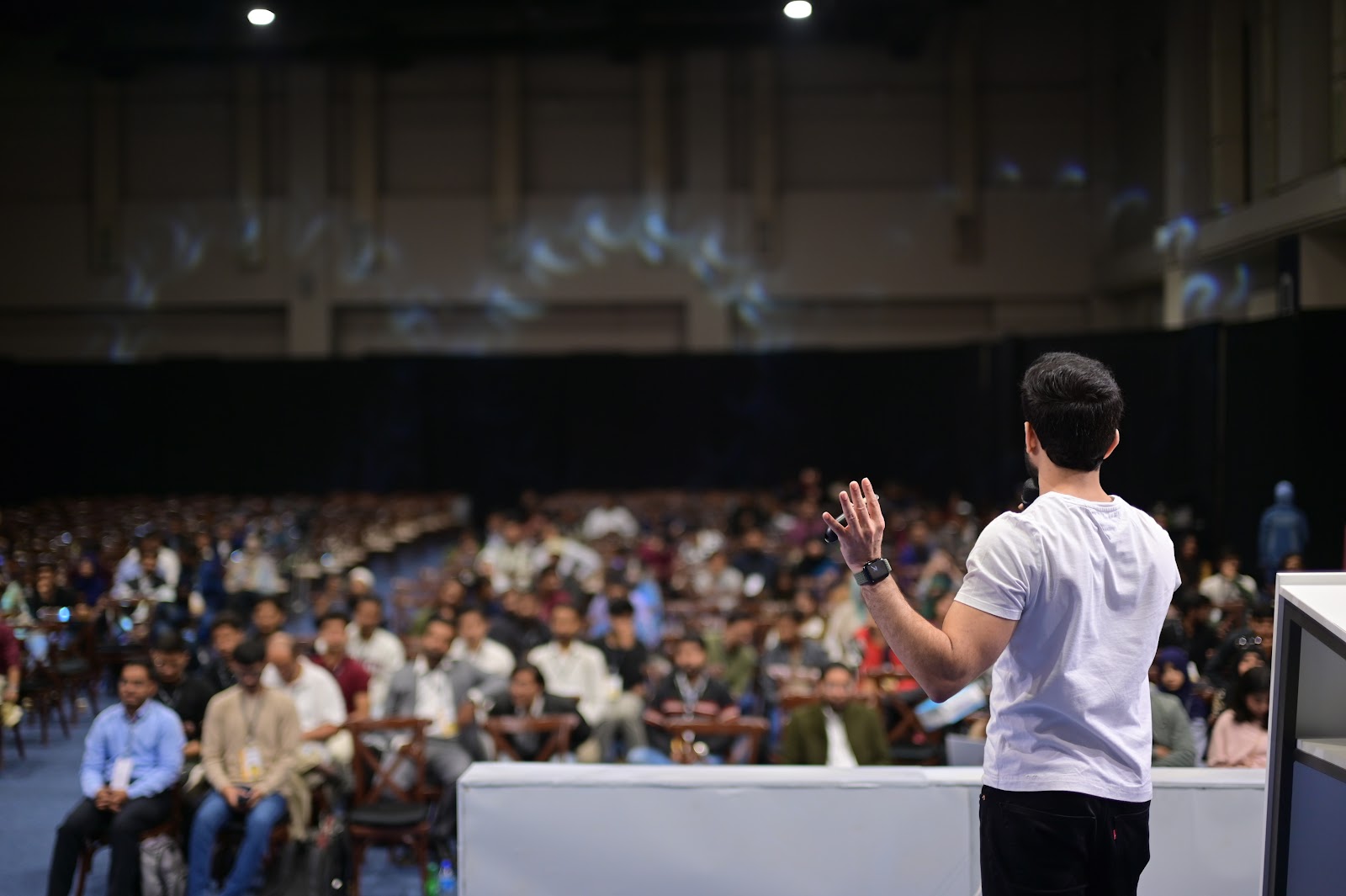 Speaker standing on stage facing blurred conference audience highlighting leadership and engagement